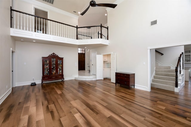 unfurnished living room with wood finished floors, ceiling fan, a high ceiling, stairs, and baseboards