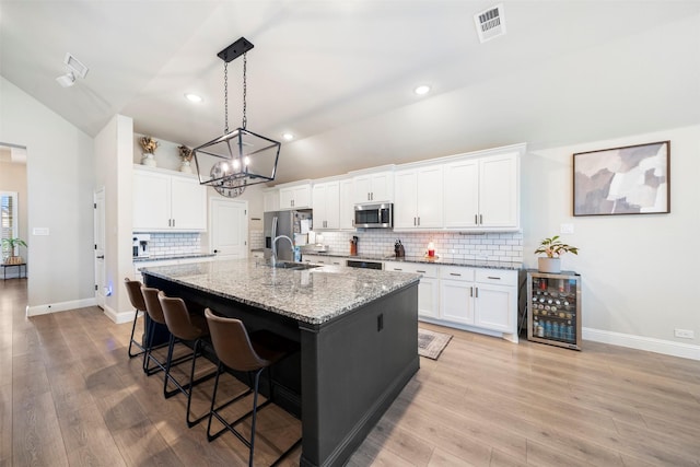 kitchen with stainless steel appliances, lofted ceiling, an island with sink, a sink, and beverage cooler