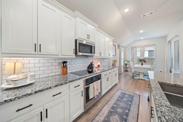 kitchen featuring stainless steel appliances, lofted ceiling, decorative backsplash, white cabinetry, and light wood finished floors