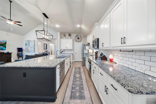 kitchen with appliances with stainless steel finishes, a sink, lofted ceiling, light wood-style floors, and white cabinets