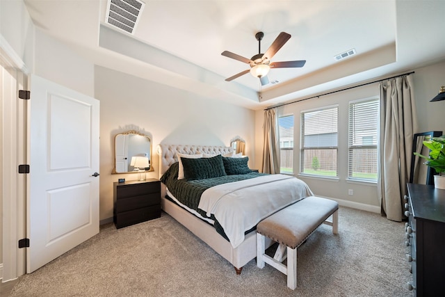 bedroom with a tray ceiling, light colored carpet, baseboards, and ceiling fan