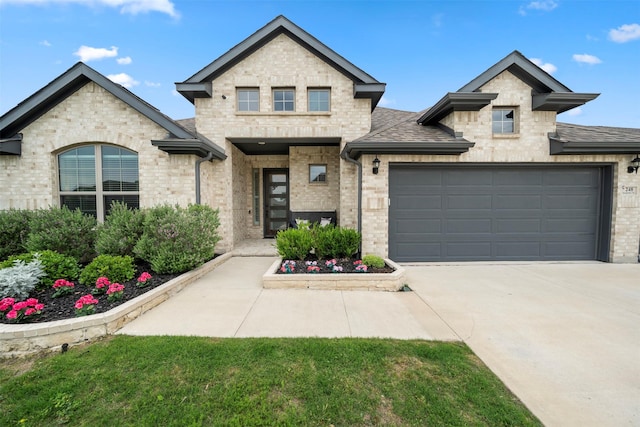 french country style house with concrete driveway, a garage, stone siding, brick siding, and roof with shingles