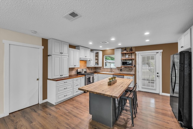 3601 Orchard Ln, Waco, TX 76705 - kitchen featuring wooden counters, stainless steel appliances, open shelves, a breakfast bar, and wood finished floors