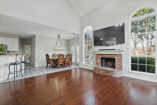 living area featuring hardwood / wood-style floors, a brick fireplace, baseboards, lofted ceiling, and a chandelier