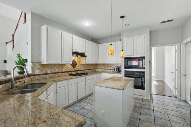 kitchen featuring black appliances, a sink, under cabinet range hood, light stone countertops, and decorative backsplash