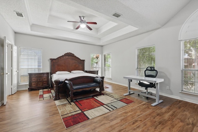 bedroom with a textured ceiling, wood finished floors, a tray ceiling, baseboards, and ceiling fan