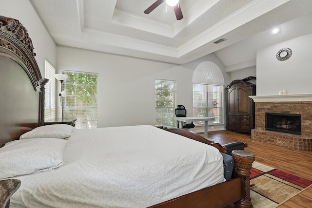 bedroom featuring wood finished floors, multiple windows, a brick fireplace, ornamental molding, and ceiling fan