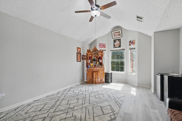 empty room with a textured ceiling, a ceiling fan, baseboards, wood finished floors, and lofted ceiling