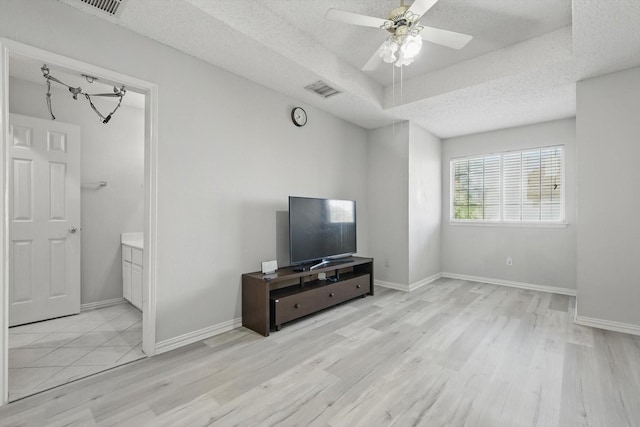 unfurnished living room featuring wood finished floors, a textured ceiling, a ceiling fan, baseboards, and a tray ceiling
