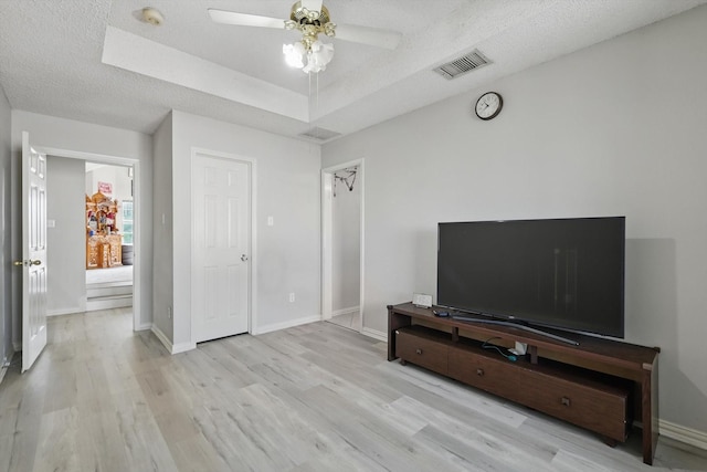 unfurnished living room with light wood-style floors, ceiling fan, a textured ceiling, baseboards, and a raised ceiling