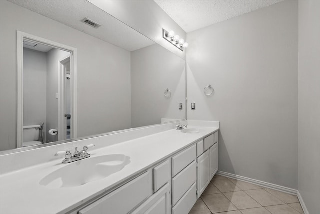 full bath with a textured ceiling, toilet, double vanity, baseboards, and tile patterned flooring