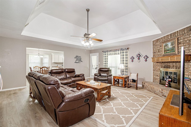 living area featuring a raised ceiling, light wood finished floors, ceiling fan, and plenty of natural light