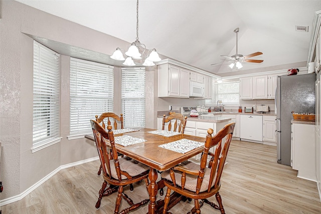 dining space featuring a textured wall, vaulted ceiling, light wood finished floors, a chandelier, and ceiling fan