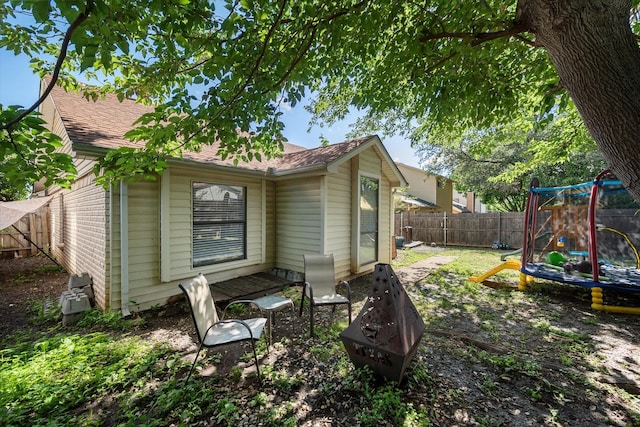 4677 Bracken Dr, Fort Worth, TX 76137 - back of house with a trampoline, a fenced backyard, roof with shingles, brick siding, and a playground