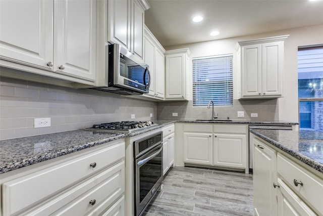 kitchen with a sink, stainless steel appliances, white cabinetry, decorative backsplash, and recessed lighting