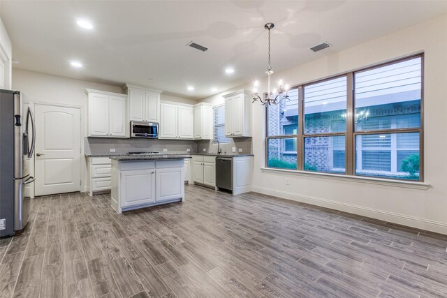 kitchen with stainless steel appliances, wood finished floors, a sink, dark countertops, and baseboards