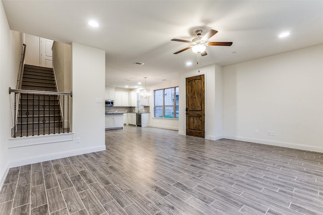 unfurnished living room featuring light wood finished floors, a ceiling fan, stairs, baseboards, and a chandelier