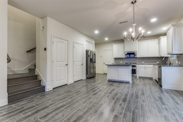 kitchen featuring appliances with stainless steel finishes, a chandelier, wood finished floors, a center island, and white cabinets