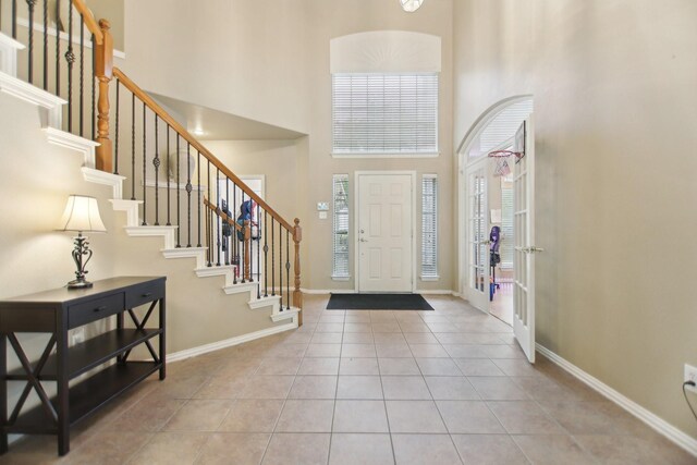 tiled entrance foyer with a towering ceiling, stairway, and baseboards