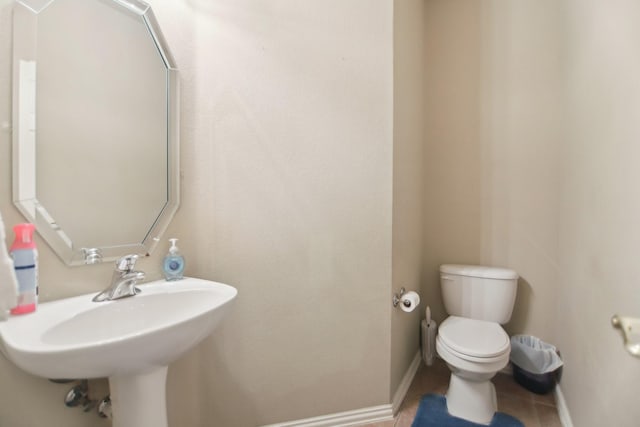 half bath with toilet, baseboards, a sink, and tile patterned floors