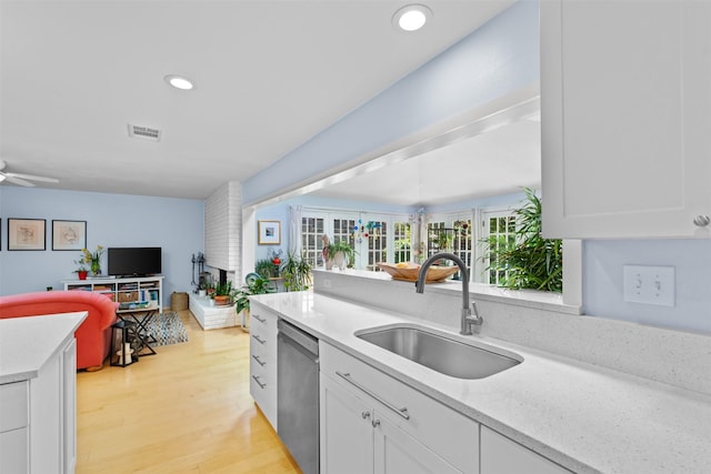 kitchen featuring a sink, open floor plan, stainless steel dishwasher, white cabinetry, and light wood finished floors
