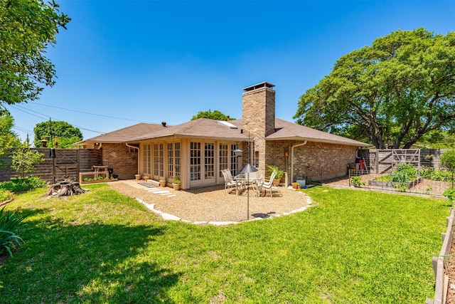 rear view of house with a patio area, a chimney, brick siding, a vegetable garden, and roof with shingles