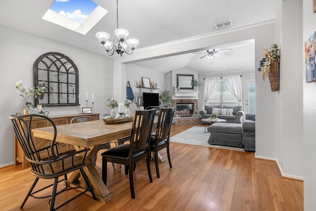 dining space featuring a brick fireplace, lofted ceiling, a skylight, light wood finished floors, and baseboards