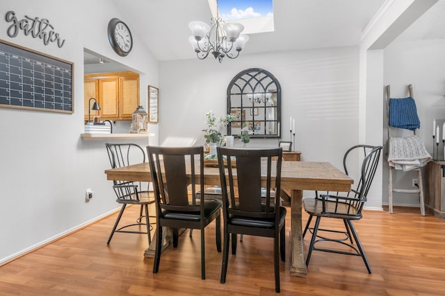 dining area featuring light wood-style floors, a chandelier, lofted ceiling, and a skylight