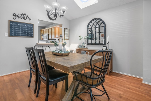 dining space with a chandelier, light wood finished floors, vaulted ceiling, a skylight, and baseboards