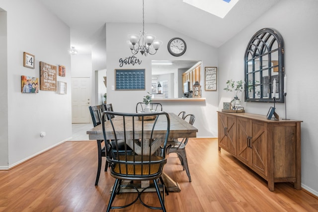 dining room with vaulted ceiling, a chandelier, light wood-style floors, a skylight, and baseboards