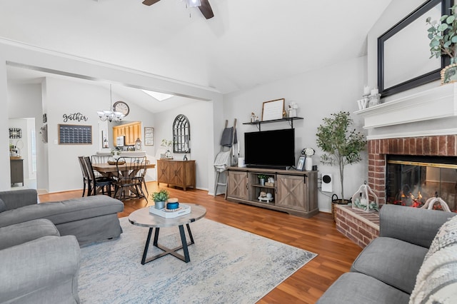 living room featuring lofted ceiling, ceiling fan, wood finished floors, a brick fireplace, and a chandelier