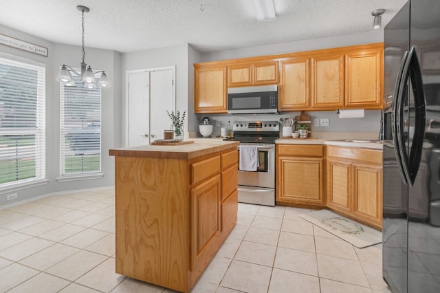 kitchen with stainless steel appliances, light countertops, a kitchen island, light tile patterned floors, and a chandelier