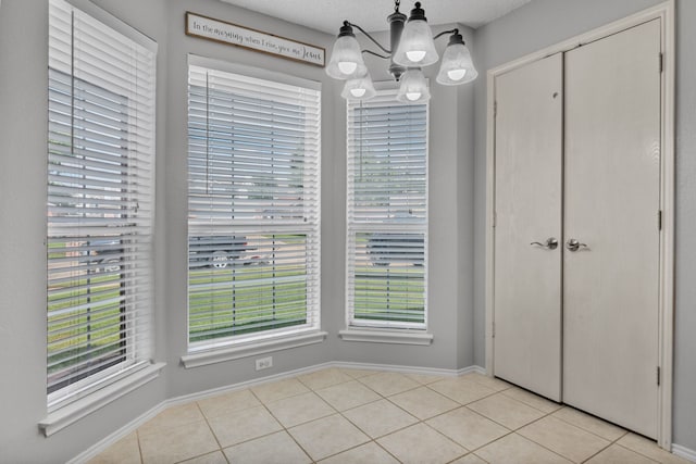 unfurnished dining area with a chandelier, light tile patterned floors, and baseboards