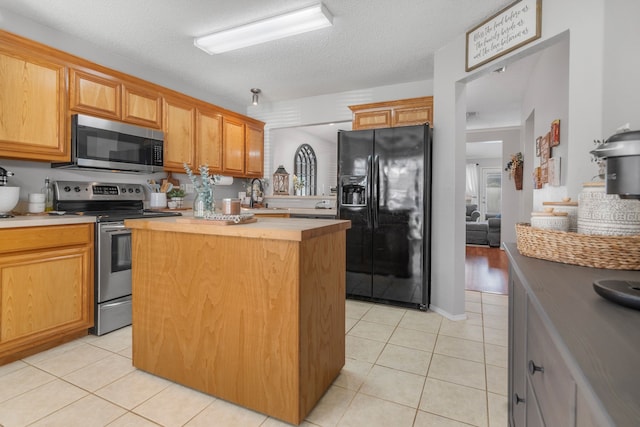 kitchen with appliances with stainless steel finishes, light tile patterned floors, a kitchen island, light countertops, and a textured ceiling