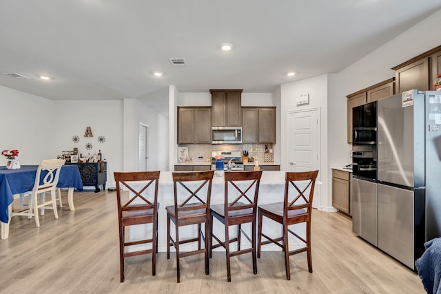 3204 Peacock Ln, Celina, TX 75009 - kitchen with stainless steel appliances, decorative backsplash, light wood-style flooring, a breakfast bar area, and light countertops