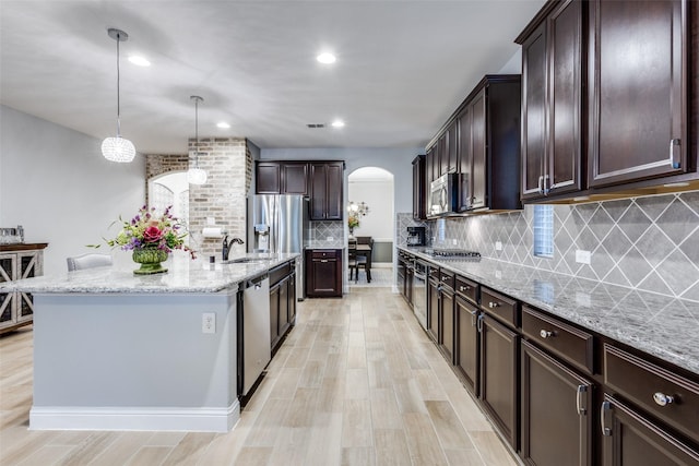 1417 Madrid Falls Dr, Mckinney, TX 75071 - kitchen featuring arched walkways, stainless steel appliances, a sink, light stone countertops, and dark brown cabinetry