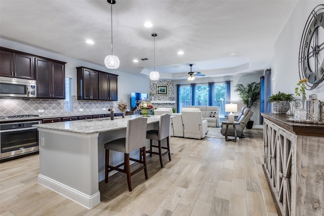 1417 Madrid Falls Dr, Mckinney, TX 75071 - kitchen featuring appliances with stainless steel finishes, light wood finished floors, backsplash, a tray ceiling, and dark brown cabinetry