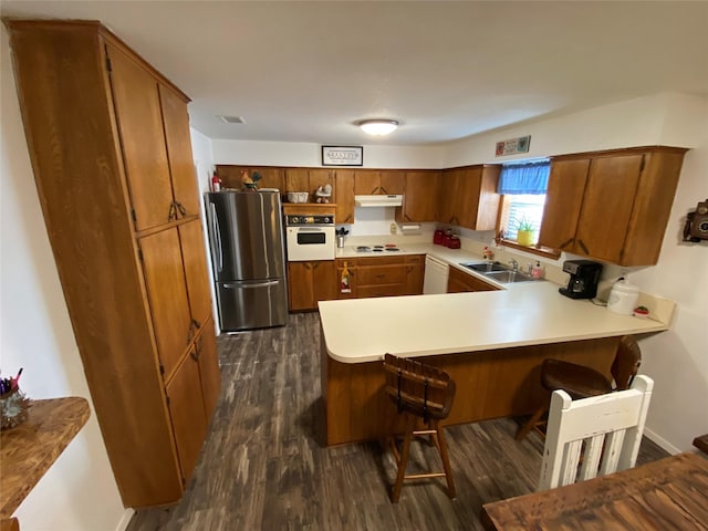 kitchen with white appliances, under cabinet range hood, a peninsula, and brown cabinetry