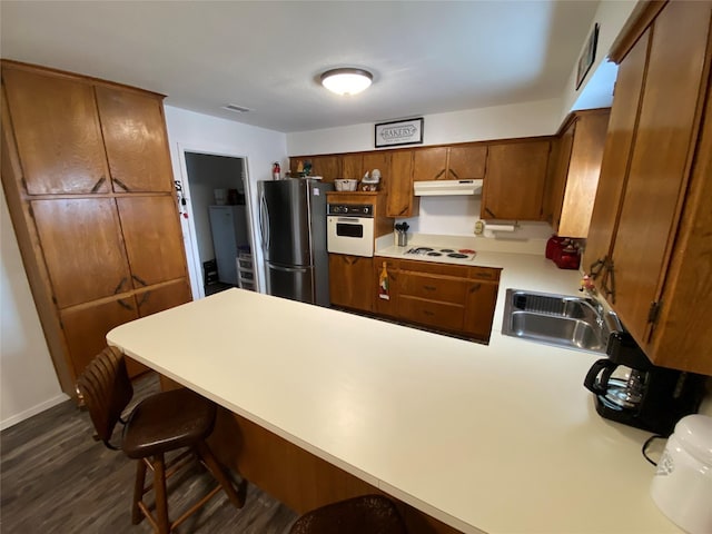 kitchen featuring white appliances, under cabinet range hood, a peninsula, brown cabinetry, and a sink