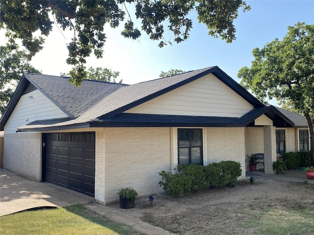 view of front facade with roof with shingles, brick siding, and a garage