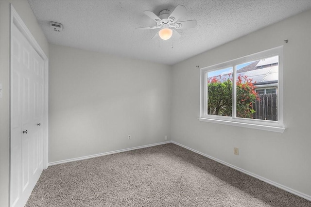 unfurnished bedroom featuring carpet floors, a textured ceiling, a closet, baseboards, and a ceiling fan