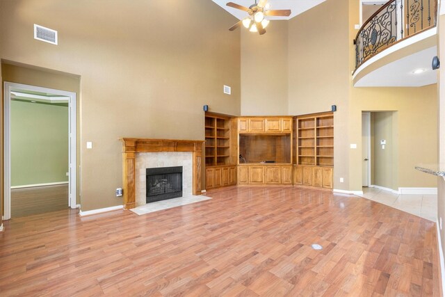 2609 Green Oak Dr, Carrollton, TX 75010 - unfurnished living room featuring a towering ceiling, a ceiling fan, baseboards, light wood-type flooring, and a tiled fireplace
