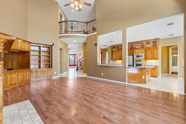 2609 Green Oak Dr, Carrollton, TX 75010 - unfurnished living room featuring ceiling fan, light wood-style flooring, stairs, a towering ceiling, and baseboards