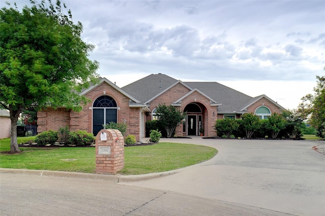 7300 Bishop Ct, Fort Worth, TX 76179 - view of front of home with brick siding, a front yard, roof with shingles, and curved driveway