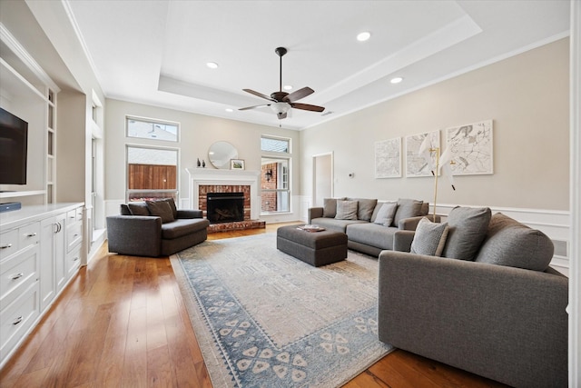 living area featuring a raised ceiling, a ceiling fan, recessed lighting, wood-type flooring, and a fireplace