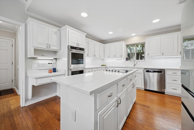 kitchen featuring appliances with stainless steel finishes, crown molding, white cabinetry, backsplash, and a sink