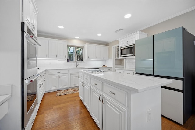 kitchen featuring stainless steel appliances, decorative backsplash, white cabinetry, crown molding, and recessed lighting
