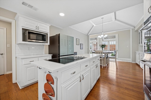kitchen featuring black electric cooktop, stainless steel microwave, vaulted ceiling, a chandelier, and healthy amount of natural light