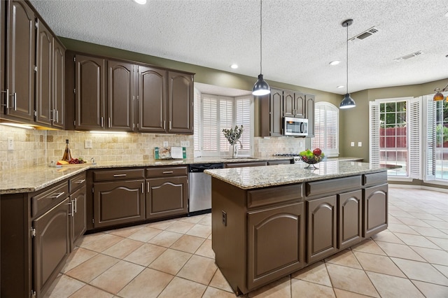 6748 Bastille Dr, Plano, TX 75024 - kitchen with appliances with stainless steel finishes, a kitchen island, a sink, tasteful backsplash, and dark brown cabinetry