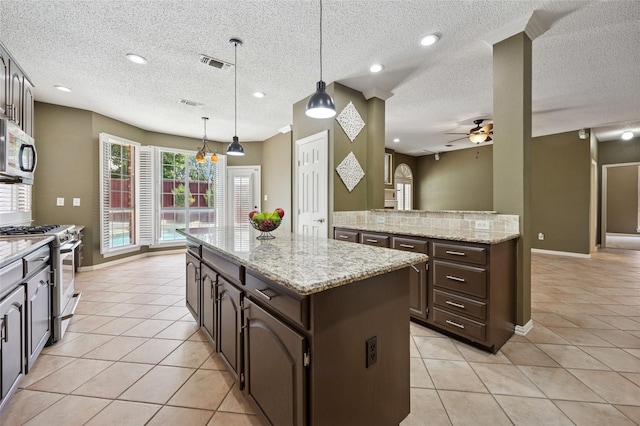 6748 Bastille Dr, Plano, TX 75024 - kitchen with appliances with stainless steel finishes, a kitchen island, light tile patterned floors, a ceiling fan, and dark brown cabinets